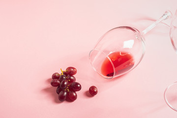 A glass of red wine on the table is turned upside down and a bunch of grapes on gentle pink...