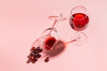 A glass of red wine on the table is turned upside down and a bunch of grapes on gentle pink...