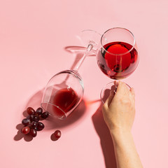 Female hand holding a glass with red wine and bunch of grapes on a gentle pink background. Selective focus. Minimalism.