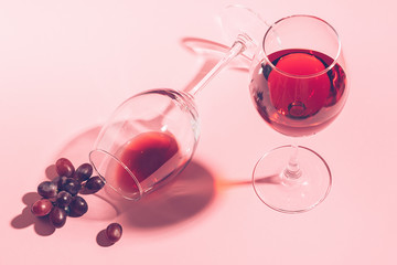 A glass of red wine on the table is turned upside down and a bunch of grapes on gentle pink...