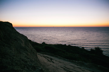 Beautiful sandy cliff and pink sky with sun rise above sea waves on tropical island. Waves in ocean at sunset light. Tranquil calm moment. Summer vacation. Copy space