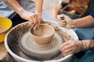 Pottery workshop. Hands of adult and child making pottery, working with wet clay closeup. Process of making bowl from clay on wheel with dirty hands. Handmade festival in summer park