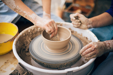 Hands of adult and child making pottery, working with wet clay closeup. Process of making bowl from...
