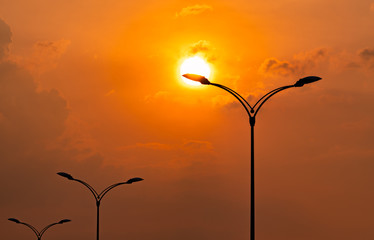 Silhouette street electric pole with beautiful orange and yellow sunset sky and clouds in the evening. Street lamp light. City road lamp post for illumination Power and energy conservation concept.