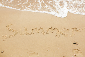 Summer sign on beach. Written summer text word on sandy beach with footprints and sea waves. Hello summer concept. Top view. Vacation, relax and travel. Copy space