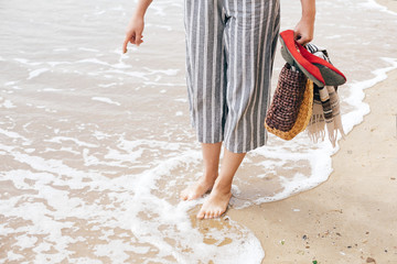 Girl trying to write summer word or sun symbol  on sandy beach at sea, but waves ruins the sign. Hello summer concept. Vacation, relax and travel. Copy space