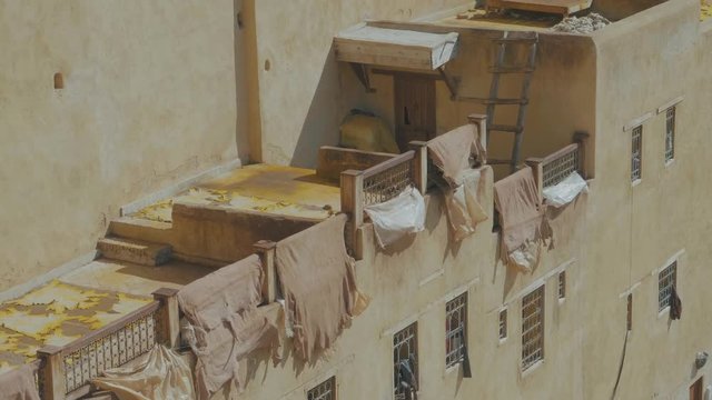Stationary camera high above the famous tannery in Fez, Morocco with cream colored building draped with large pieces of dyed materials hanging from balconies to dry