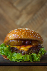 Burger, hamburger sandwich with cutlet of minced meat, melted cheese, berry cherry and pear. Side view on a wooden backdrop and light wooden board.