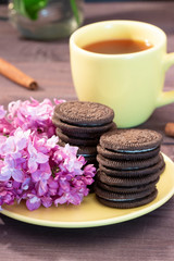 Yellow cup of tea with chocolate biscuits with a sprig of lilac and cinnamon. Tea still life yellow service, dessert