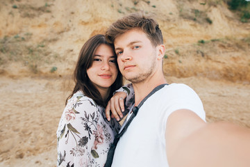 Stylish hipster couple taking selfie on beach at sandy cliff at sea. Summer vacation. Portrait of...
