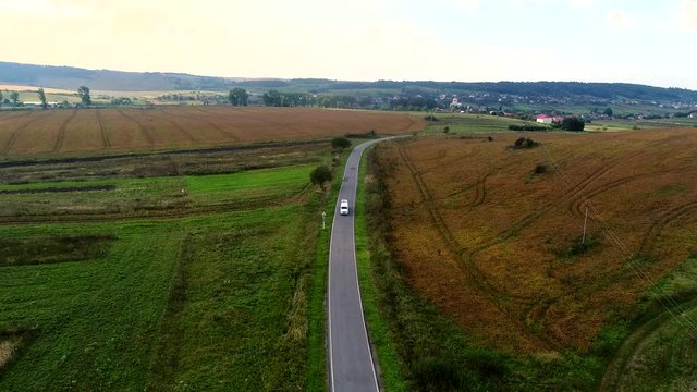 Aerial view of white car driving on country road. White limousine car moving of a Road between Green and Yellow Fields.