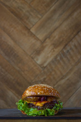 Burger, hamburger sandwich with cutlet of minced meat, melted cheese, berry cherry and pear. Side view on a wooden backdrop and light wooden board.