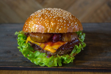 Burger, hamburger sandwich with cutlet of minced meat, melted cheese, berry cherry and pear. Top view on a wooden backdrop and light wooden board.
