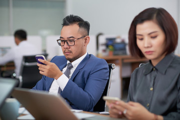 Asian business people sitting and using their mobile phones during a business meeting at office