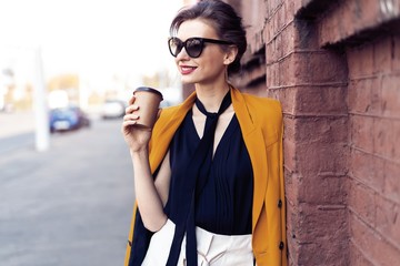 Portrait fashion woman in sunglasses walking on street . She wears yellow jacket, smiling to side.