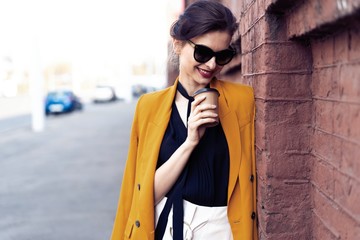 Fototapeta premium Portrait fashion woman in sunglasses walking on street . She wears yellow jacket, smiling to side.