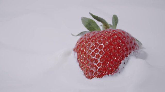 Single straberry falling into milk, slow motion shot on Red