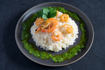 Risotto with shrimps, parsley and green sauce on a gray plate on a dark gray background with copy space. Italian food