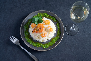 Risotto with shrimps, parsley, green sauce and a glass of white wine on a gray plate on a dark gray background with copy space. Italian food
