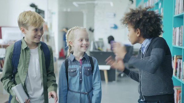 Group of three diverse elementary students, two boys and girl, walking along corridor and having fun discussing school day emotionally