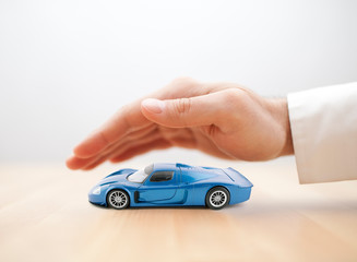 Car insurance concept with blue car toy covered by hand