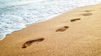 Closeup photo of calm sea waves washing off human footprints on wet sand at sandy sea beach