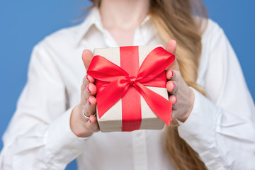 Woman in white shirt holding a box with a gift with a red ribbon, front view, close up