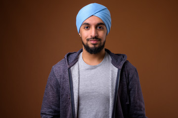 Young bearded Indian Sikh man wearing turban against brown backg