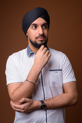 Fototapeta na wymiar Young bearded Indian Sikh man wearing turban against brown backg