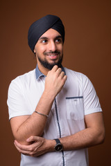 Young bearded Indian Sikh man wearing turban against brown backg