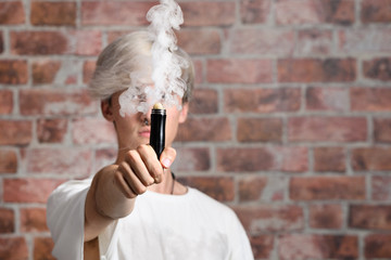 Vaper Smoke outdoor electronic cigarette near the brick wall. Young man smoking big cloud of steam