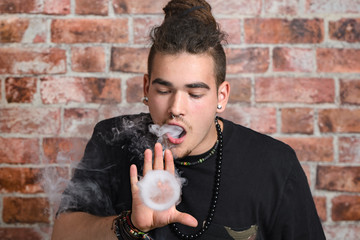 Vaper Smoke outdoor electronic cigarette near the brick wall. Young man smoking big cloud of steam