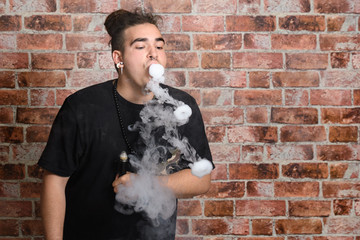 Vaper Smoke outdoor electronic cigarette near the brick wall. Young man smoking big cloud of steam