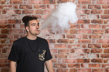 Vaper Smoke outdoor electronic cigarette near the brick wall. Young man smoking big cloud of steam
