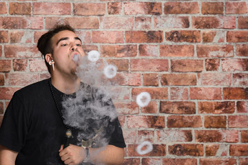 Vaper Smoke outdoor electronic cigarette near the brick wall. Young man smoking big cloud of steam