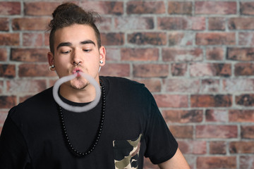 Vaper Smoke outdoor electronic cigarette near the brick wall. Young man smoking big cloud of steam