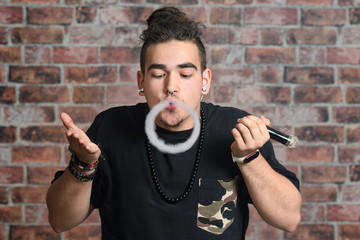 Vaper Smoke outdoor electronic cigarette near the brick wall. Young man smoking big cloud of steam