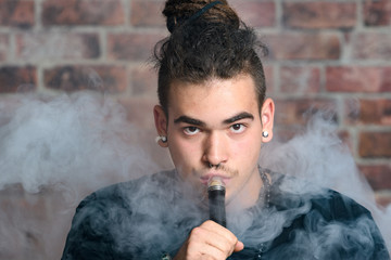 Vaper Smoke outdoor electronic cigarette near the brick wall. Young man smoking big cloud of steam