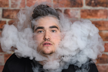 Vaper Smoke outdoor electronic cigarette near the brick wall. Young man smoking big cloud of steam