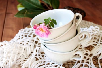 Tazas de porcelana en color blanco con rosa silvestre en tapete de ganchillo
