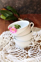 Tazas de porcelana color blanco con rosa silvestre sobre tapete de ganchillo