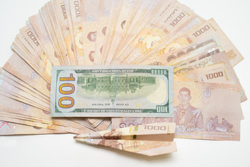 a stack of Thai baht and a hundred dollar on a white table with a plane.