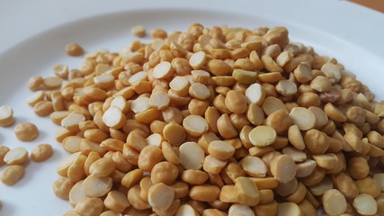 Heap of yellow split chickpeas in white plate background.