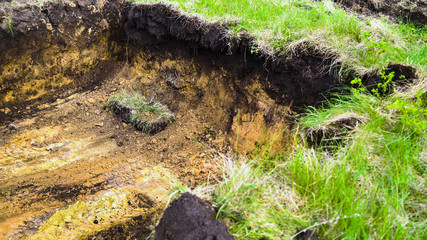 muddy trench dug in brown soil with green grass on foreground