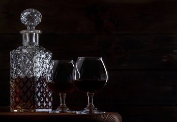 Brandy or cognac in glasses and a decanter on a brown wooden background