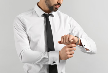 Fashionable young man looking at his watch on grey background