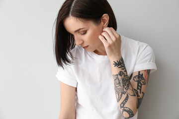 Stylish tattooed woman on light background