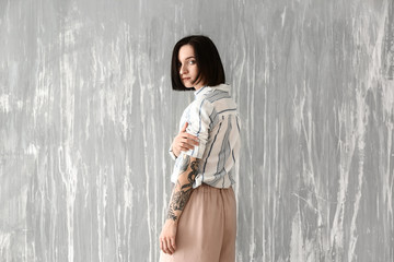 Fototapeta premium Beautiful tattooed woman near grunge wall