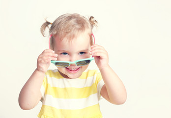 Child ghirl wearing sun glasses summer yellow background.