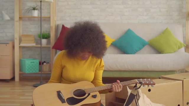 Portrait cheerful african woman with an afro hairstyle unpacks a new guitar slow mo